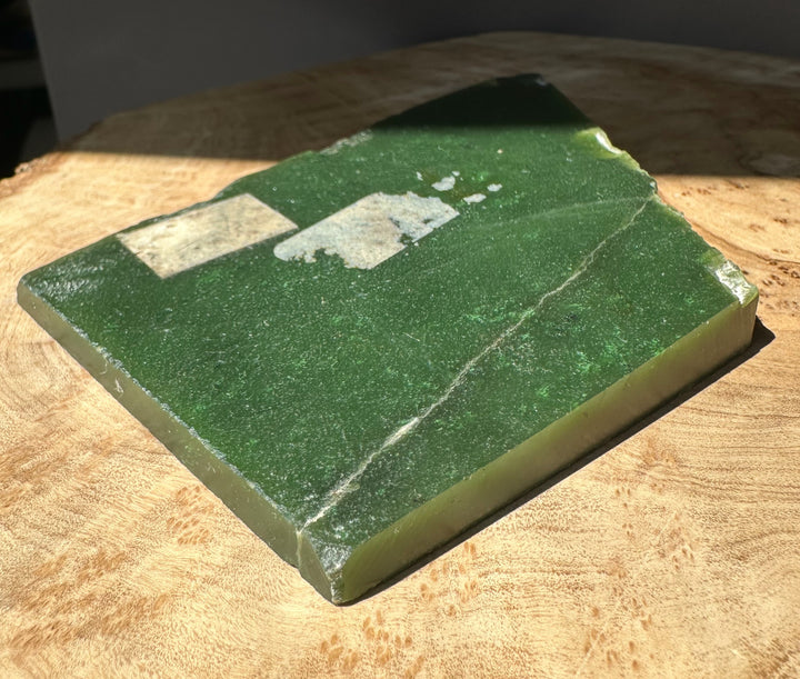 A Grade Canadian Jade Slab in deep green rests on a wooden surface with pale mineral patches.