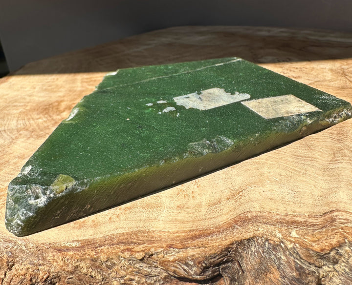 Close-up of a jade slab held by a finger, showing a smooth dark green surface and cut edge.