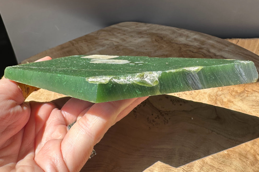 Hand holds a thick green jade slab with chipped white area along the edge