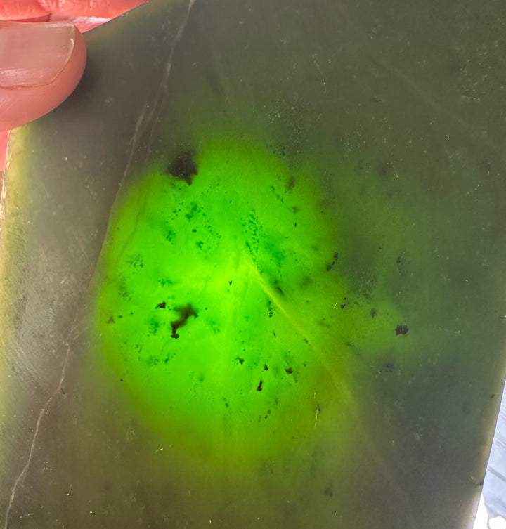 Close-up of a jade slab with dark green color and small dark specks, seen near a corner.