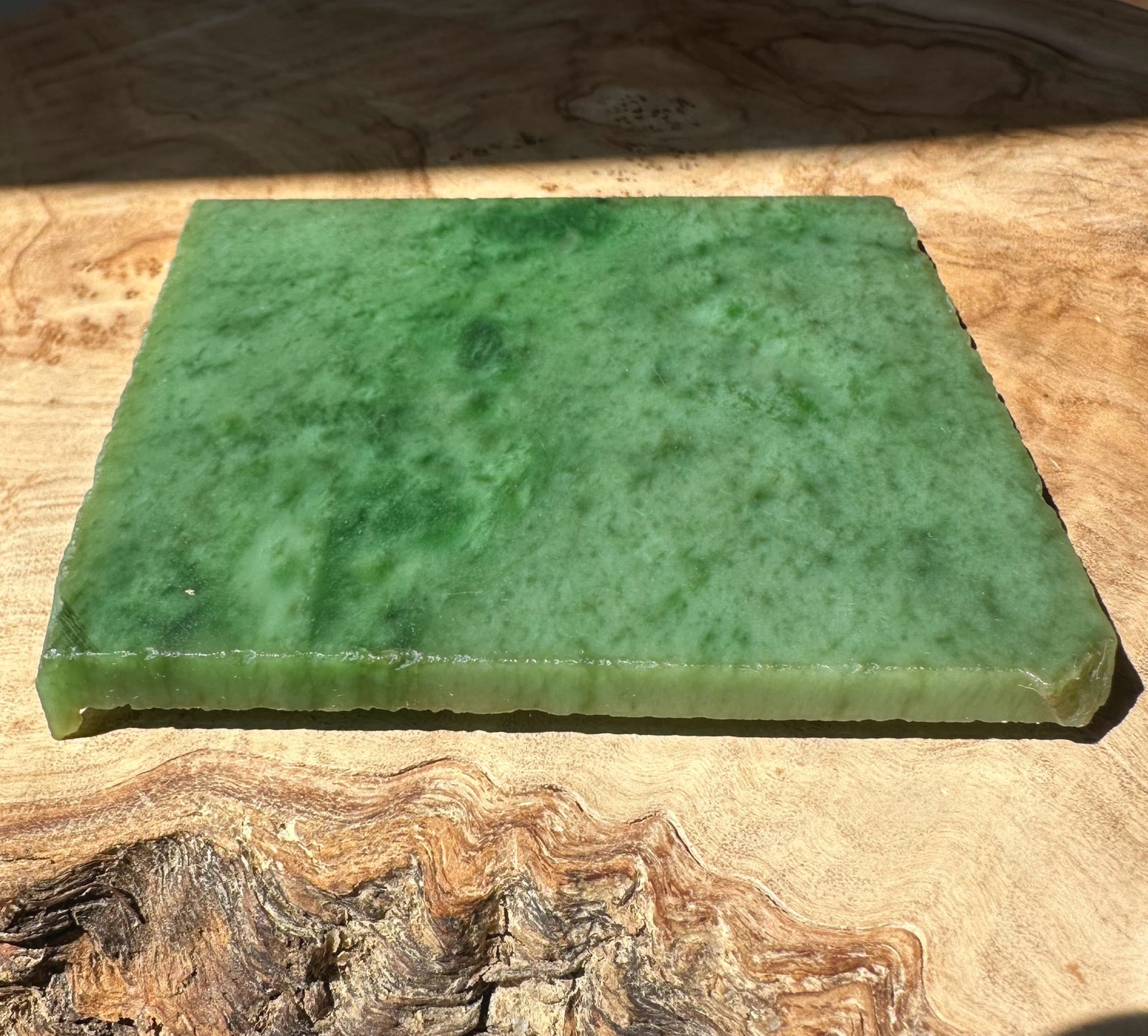 Green A+ Siberian nephrite jade slab resting on a wooden surface.