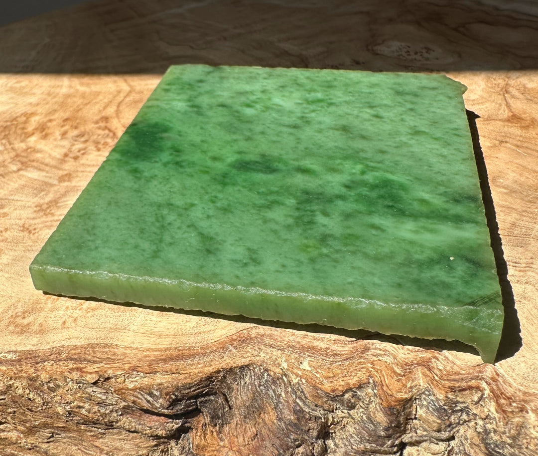 A+ Siberian nephrite jade slab in bright green resting on a wooden surface
