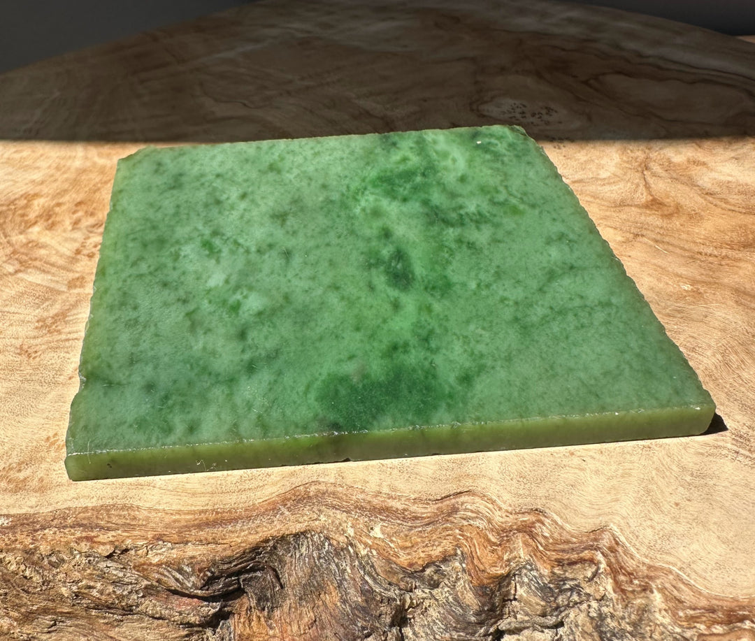 Green nephrite jade slab on a wooden surface with sunlit highlight and rough edge