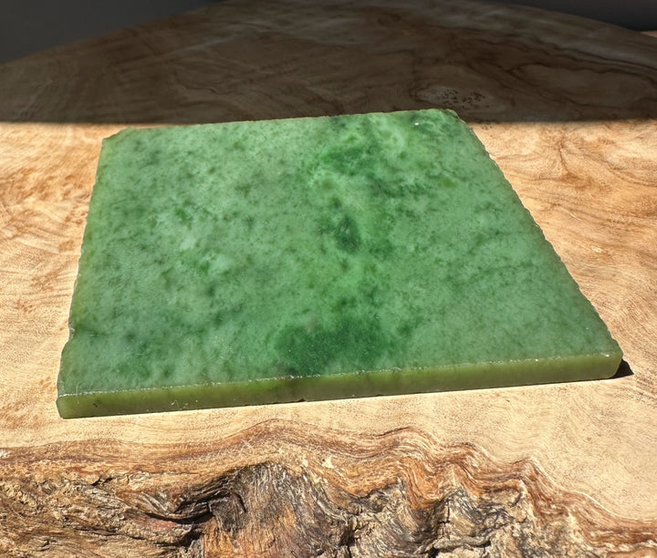 Green nephrite jade slab on a wooden surface with sunlit highlight and rough edge