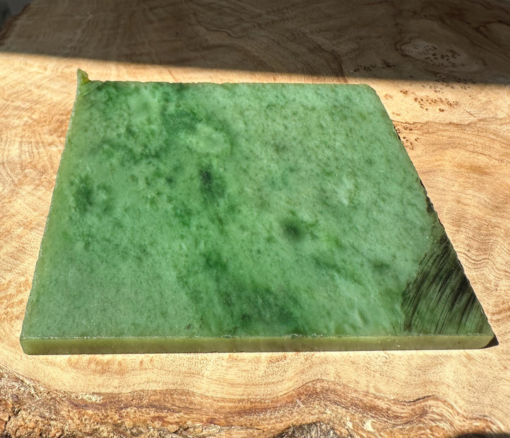 Green nephrite jade slab resting on a wooden surface with rough edges