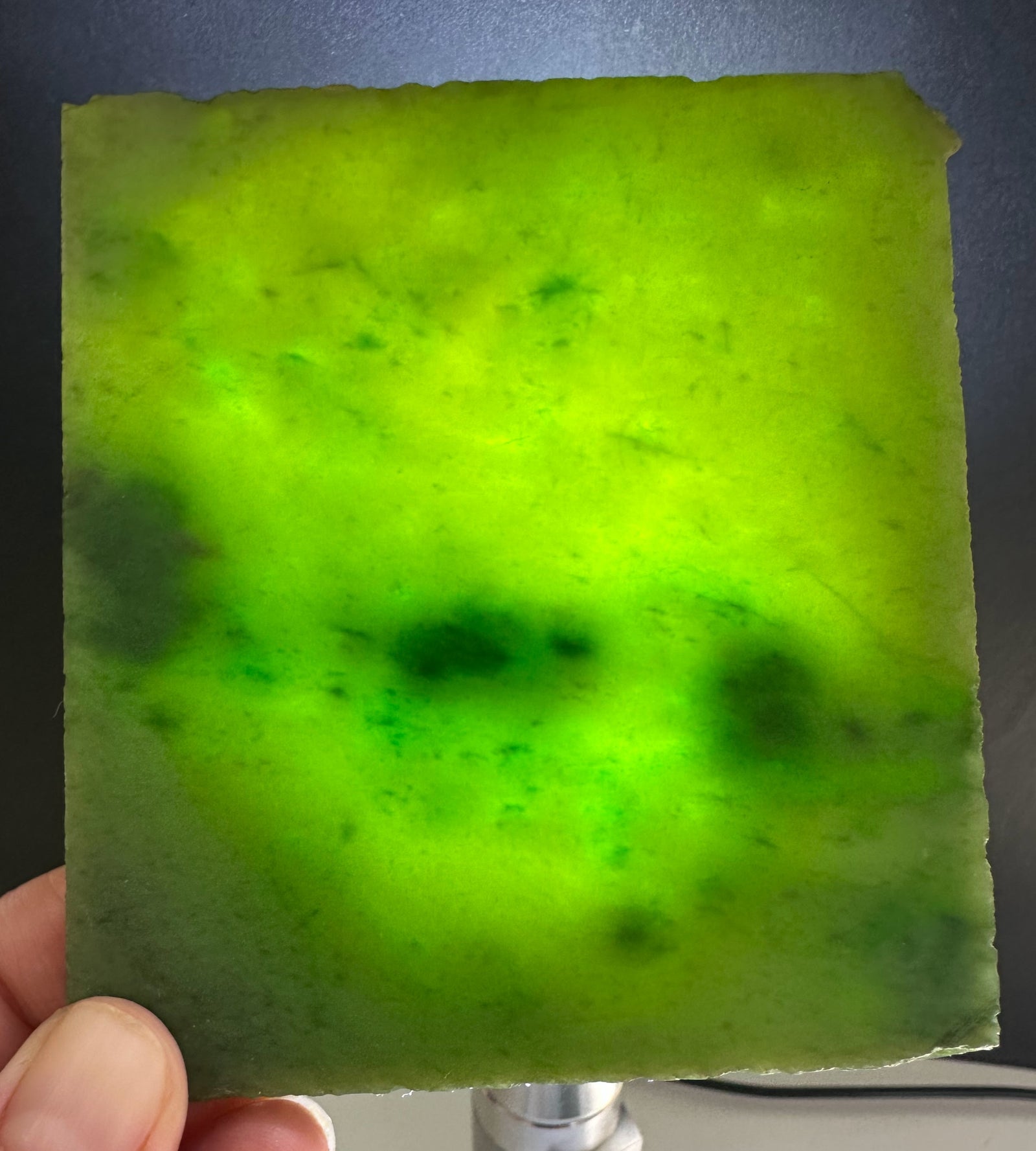 A+ Siberian nephrite jade slab in bright neon green held by fingers