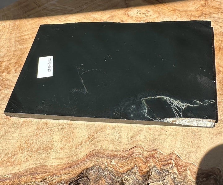 Black Wyoming Jade slab on a wooden surface with a white WYOMING label.