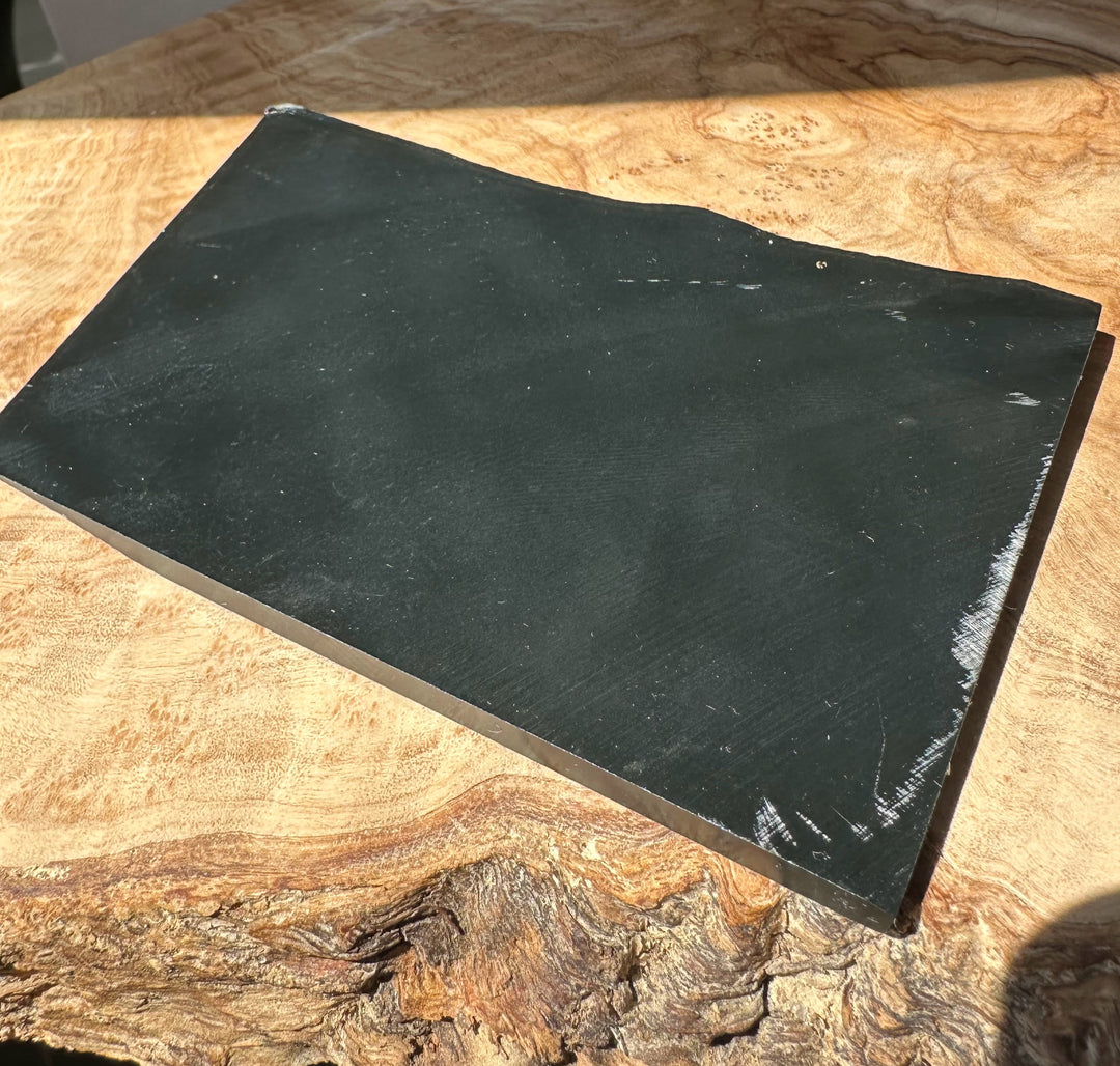 Black Wyoming jade slab with smooth dark surface and chipped edge on wooden background