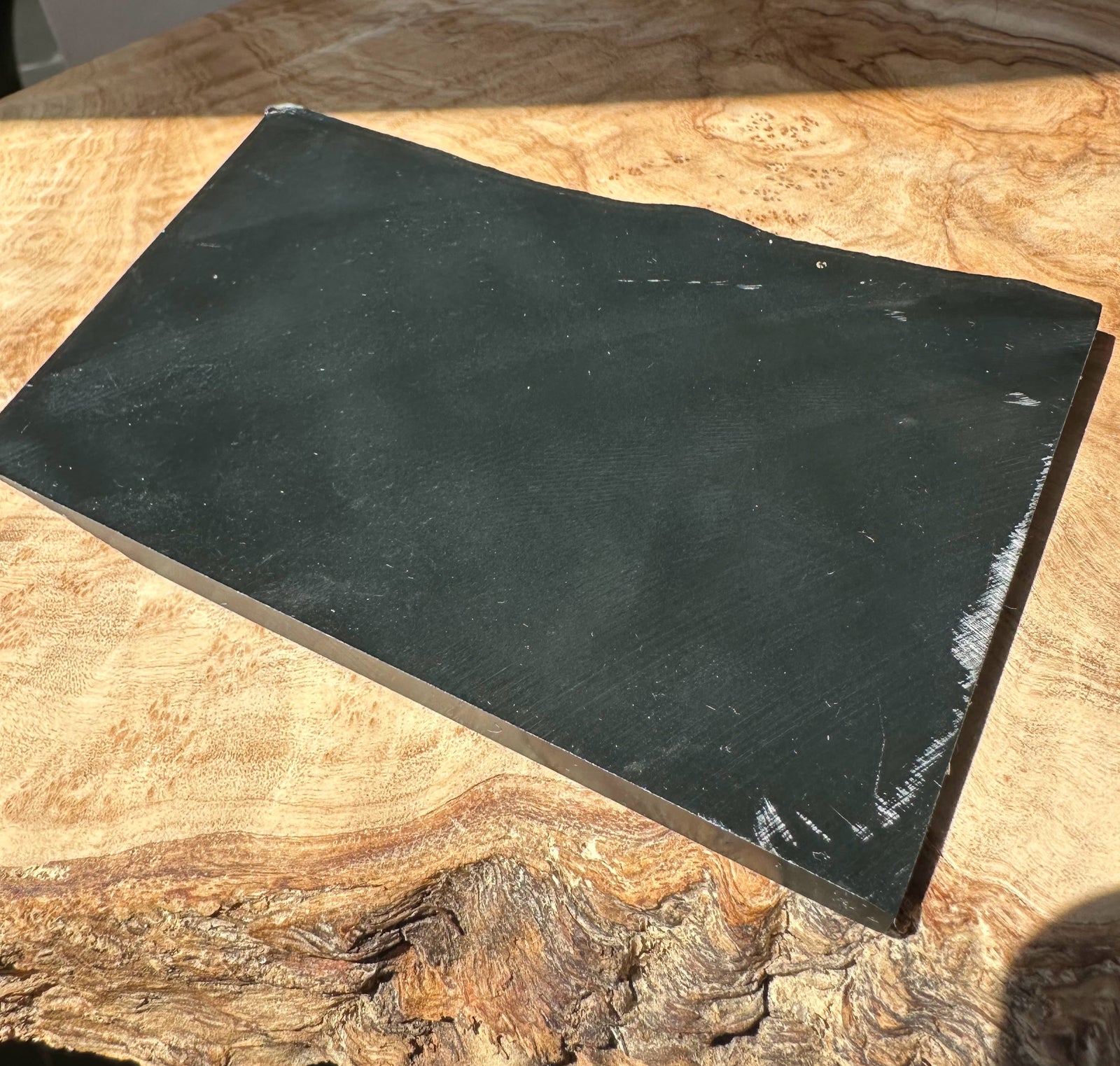 Black Wyoming jade slab with smooth dark surface and chipped edge on wooden background