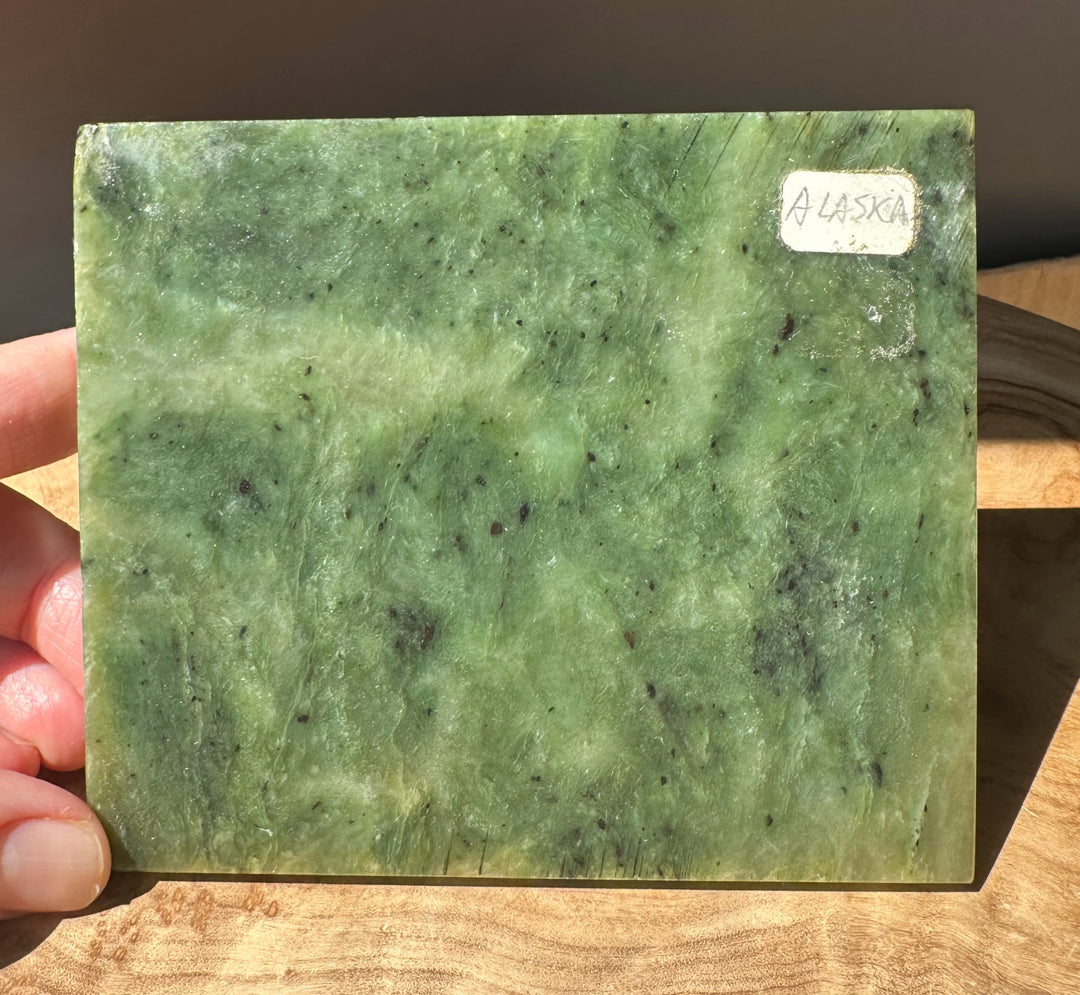 Green Alaska jade slab held by fingers on the left with a white Alaska label on the right