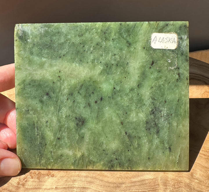 Green Alaska jade slab held by fingers on the left with a white Alaska label on the right