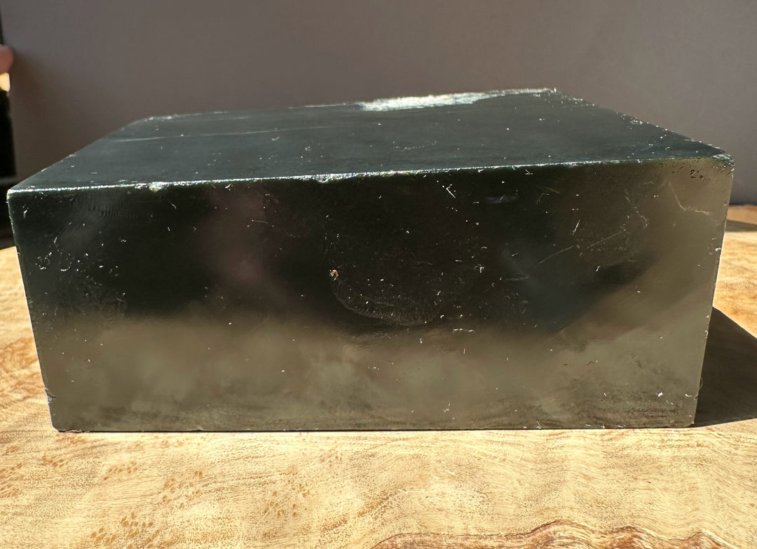 Wyoming slate block with a smooth dark face and pale edge showing subtle markings on a wooden surface