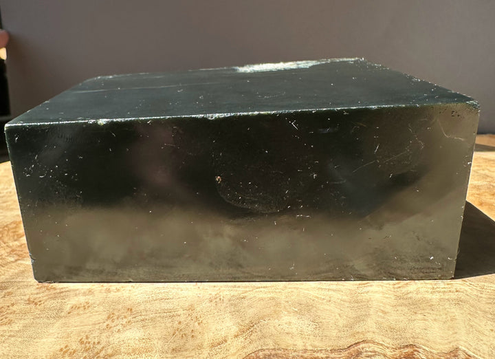 Wyoming slate block with a smooth dark face and pale edge showing subtle markings on a wooden surface