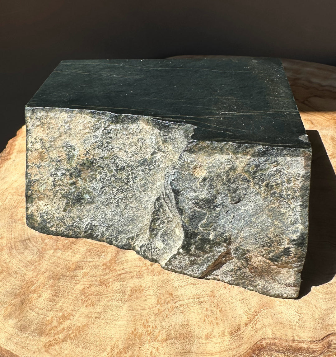 Dark green Wyoming slab with lighter veining and rough edge on a wooden surface