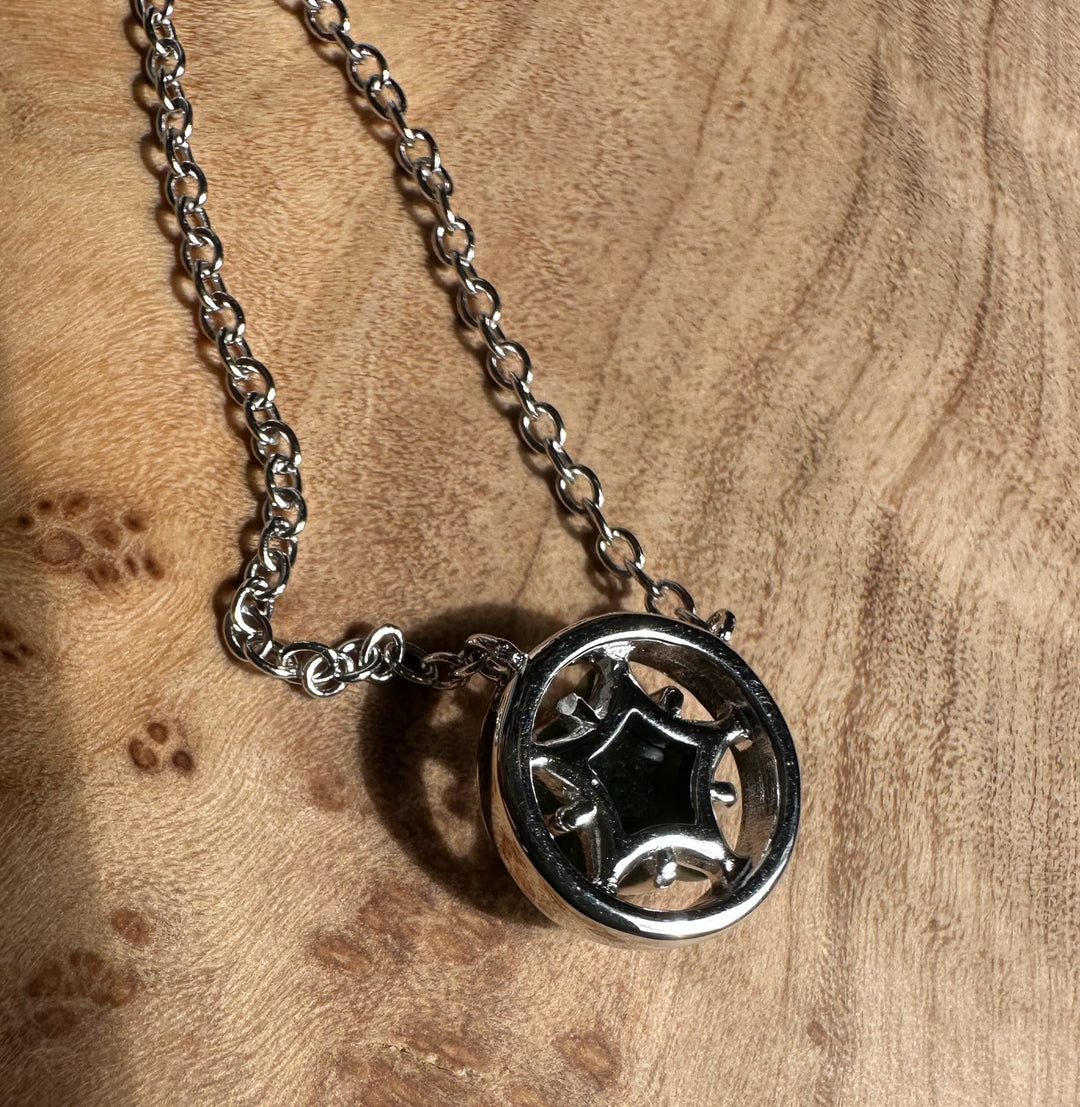 Circular silver pendant with a star shaped openwork design hanging on a silver chain.