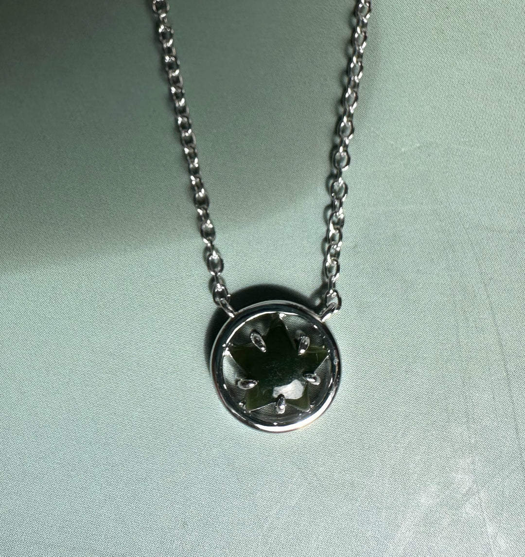 Green jade centerpiece in a round silver pendant with star shaped prongs on a silver chain.