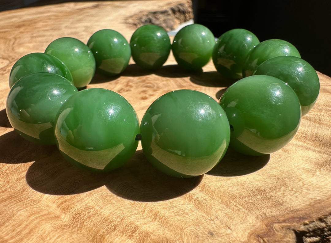 Green jade bracelet with 18mm glossy beads laid on a wooden surface