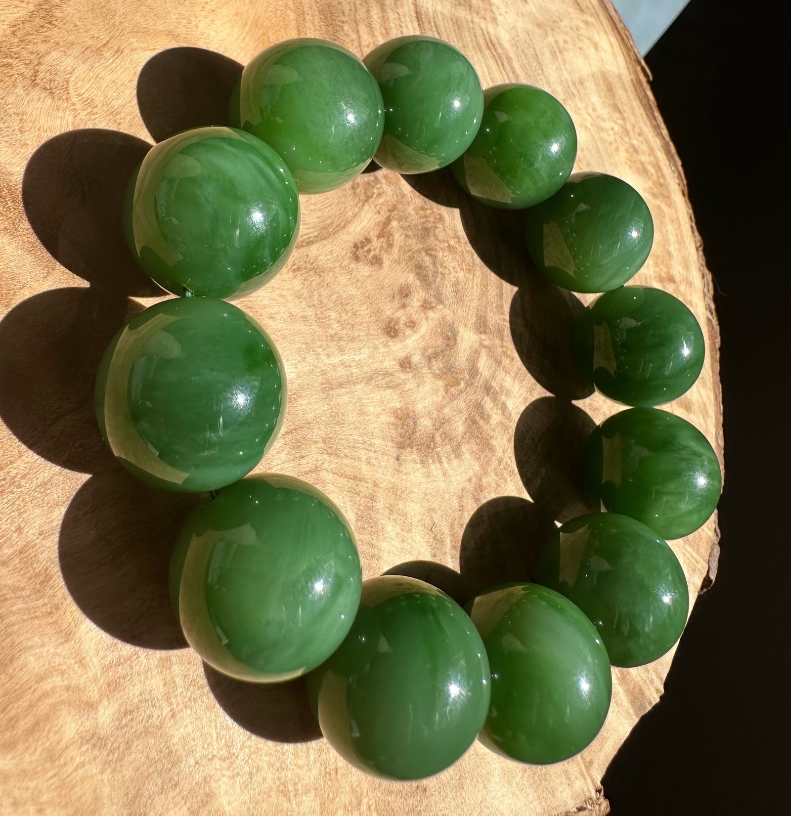 Top-down view of a circular bracelet made from large green jade beads resting on wood