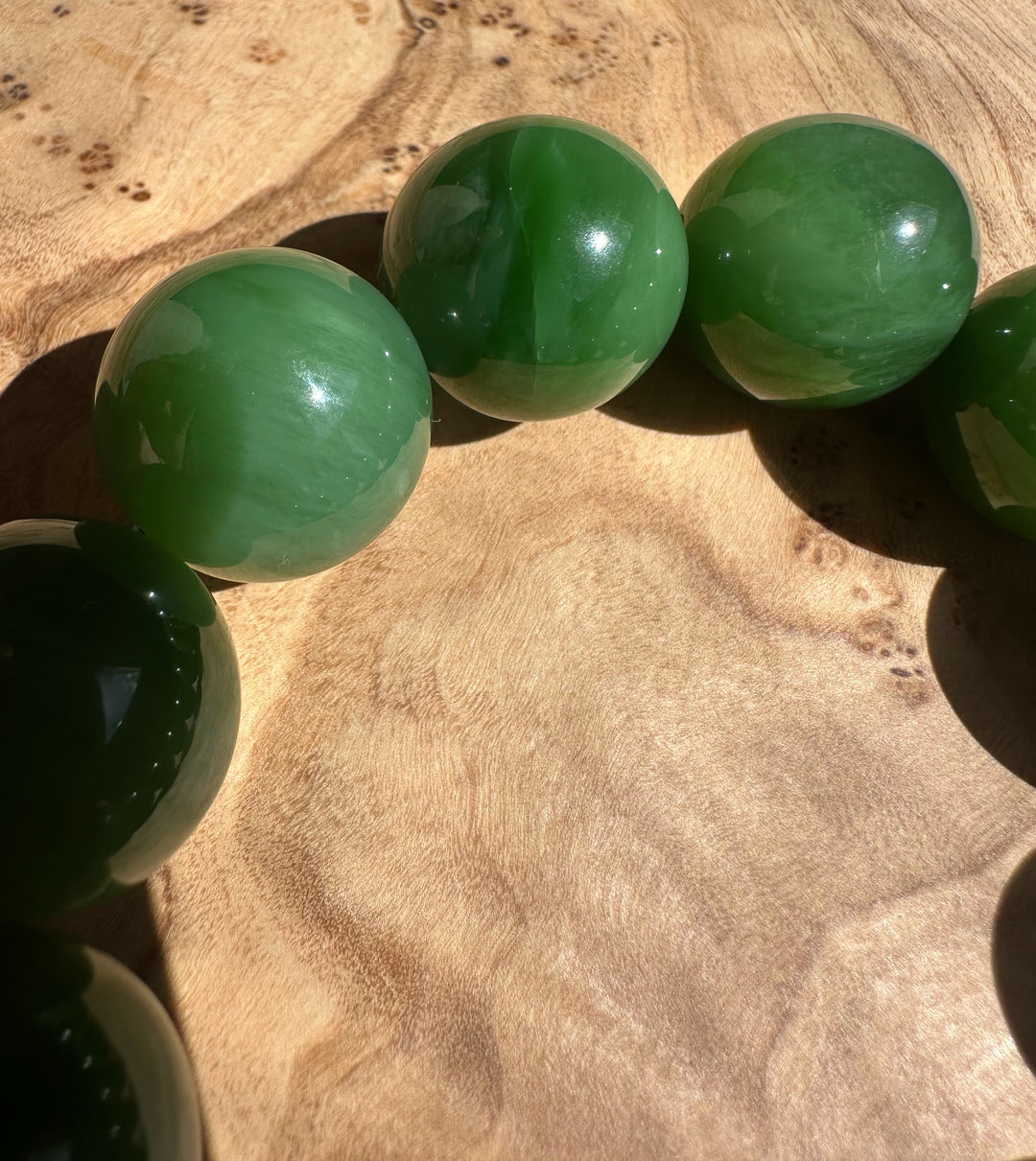 Close-up of glossy green 18mm beads resting on a wooden surface.