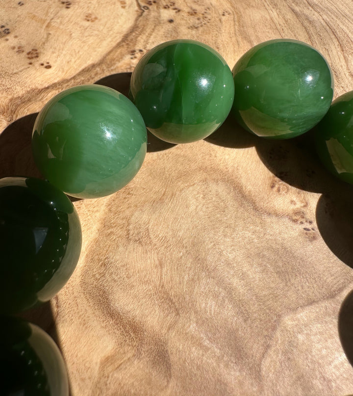 Close-up of glossy green 18mm beads resting on a wooden surface.