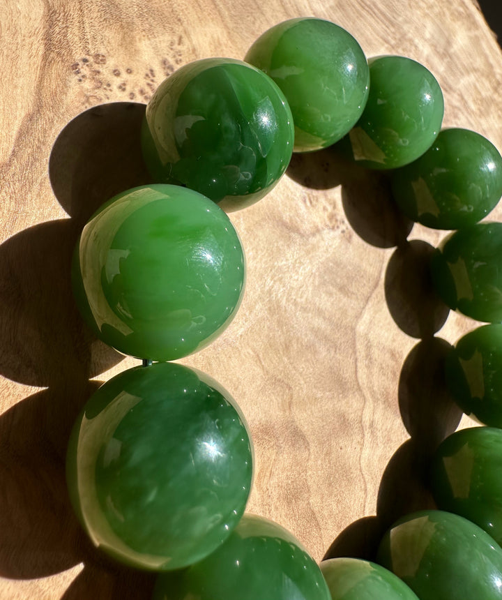 Close up of glossy green 18mm Siberian Bead Bracelet beads on a wooden surface