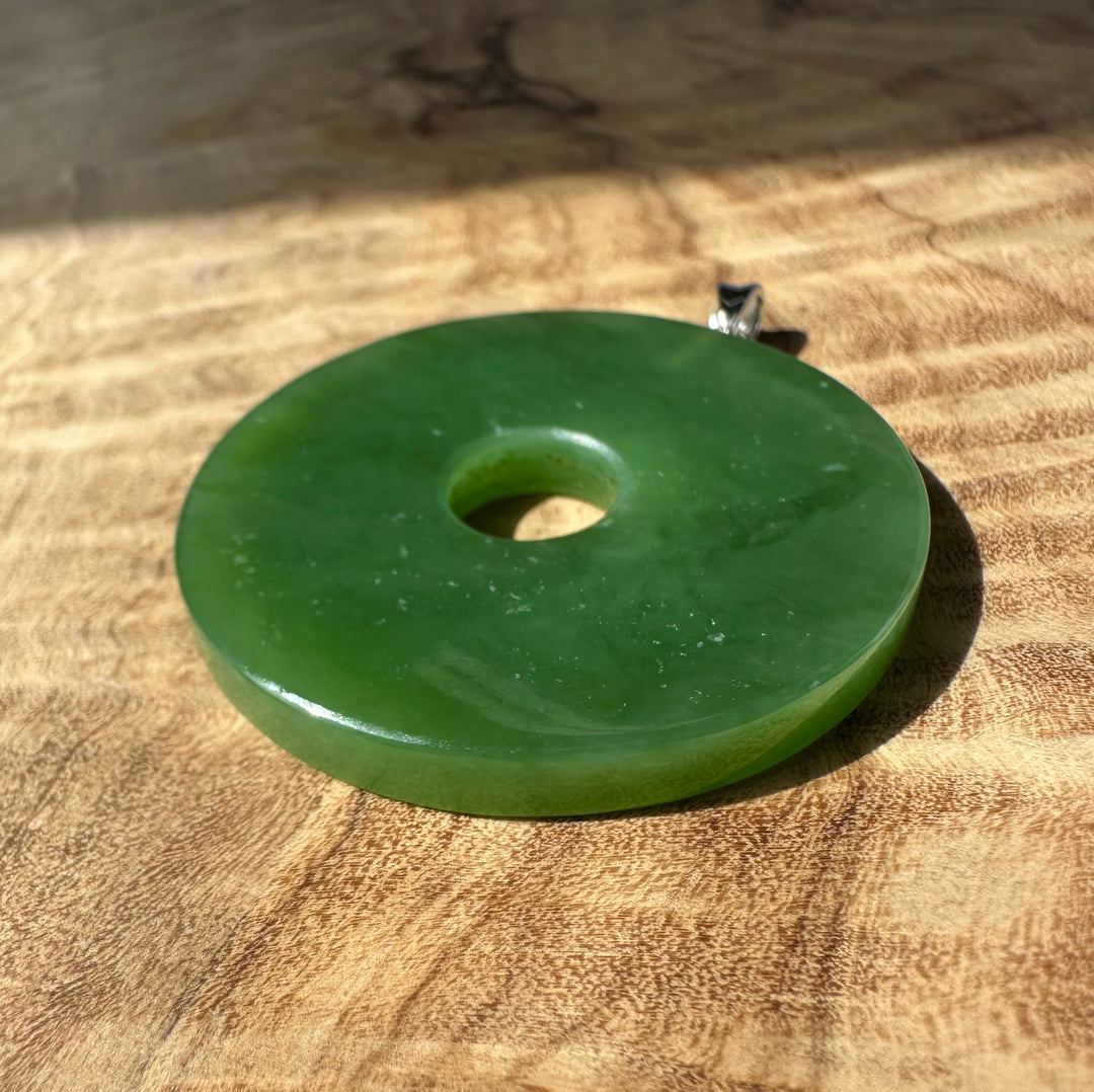 Siberian Jade Disc 40mm pendant with silver bail on a silver chain hanging in a dim indoor setting.