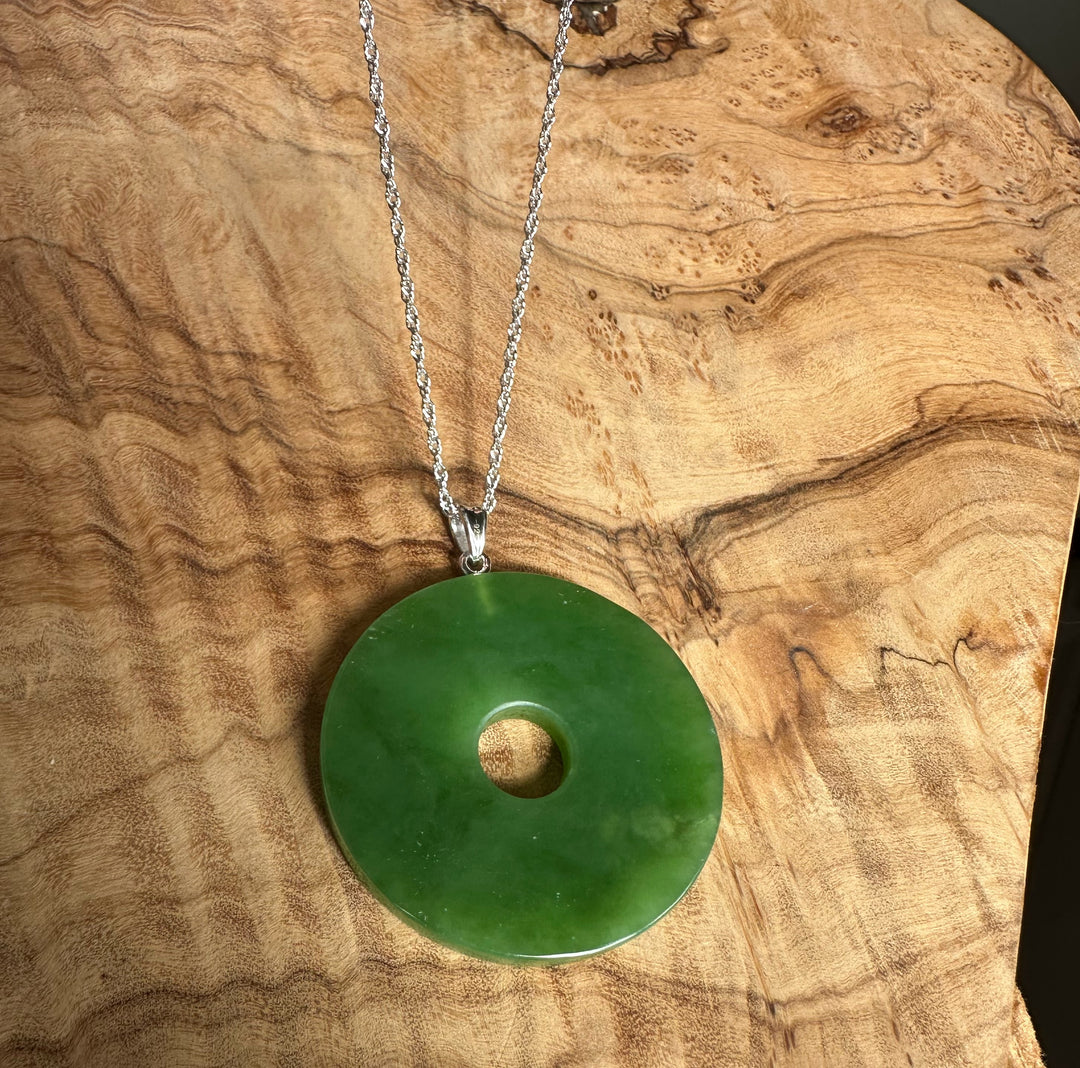 40mm Siberian Jade Disc pendant with silver chain resting on a wood grain surface.