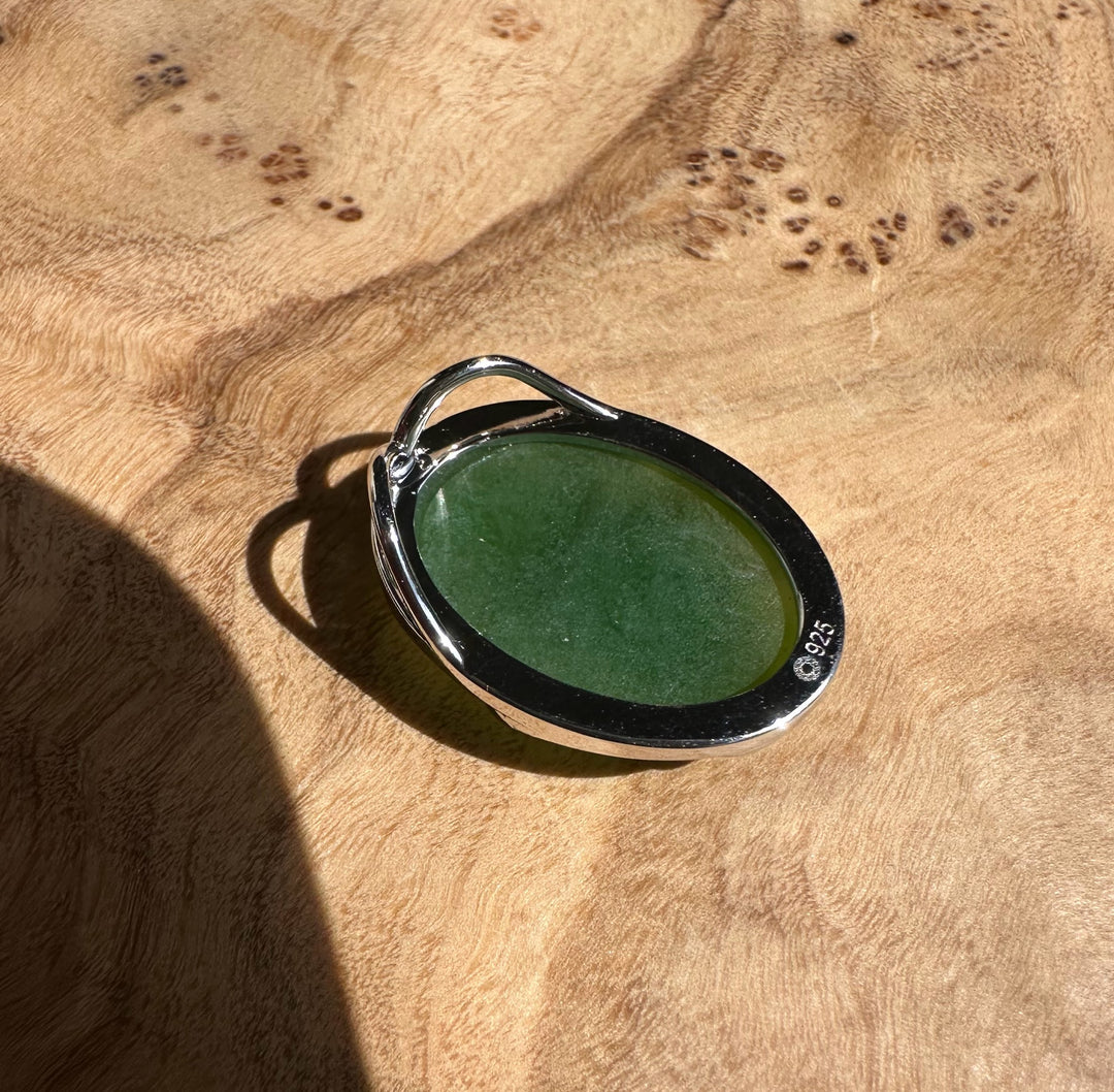 Bright Green Canadian Jade Pendant in a silver oval setting with bail on a wooden surface.