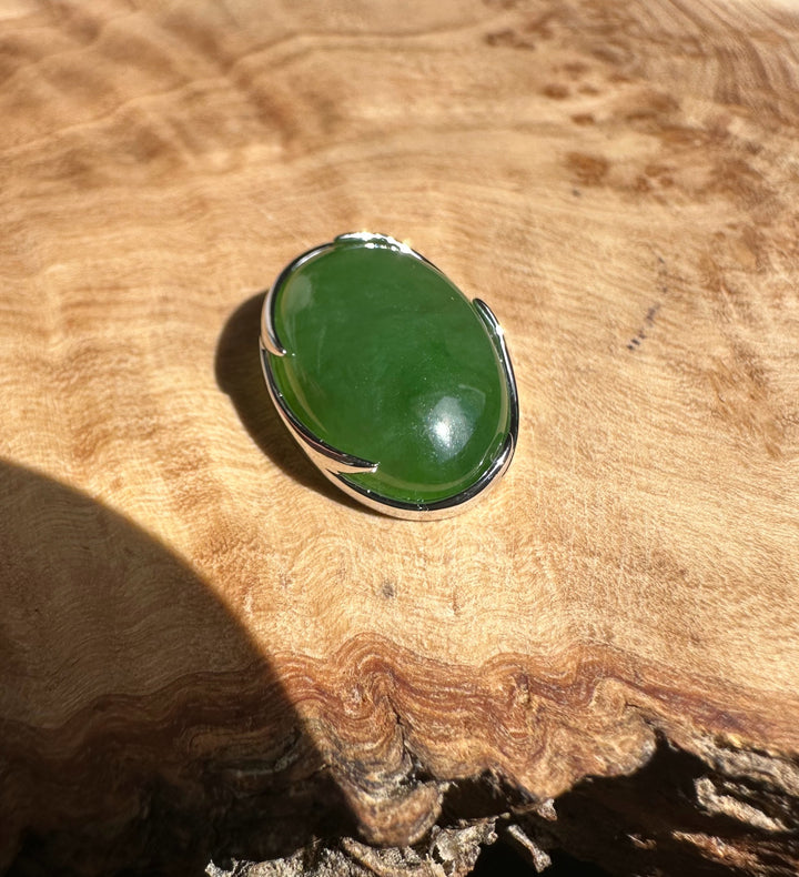 Close up of bright green Canadian jade pendant in a silver bezel with bail on wood background.