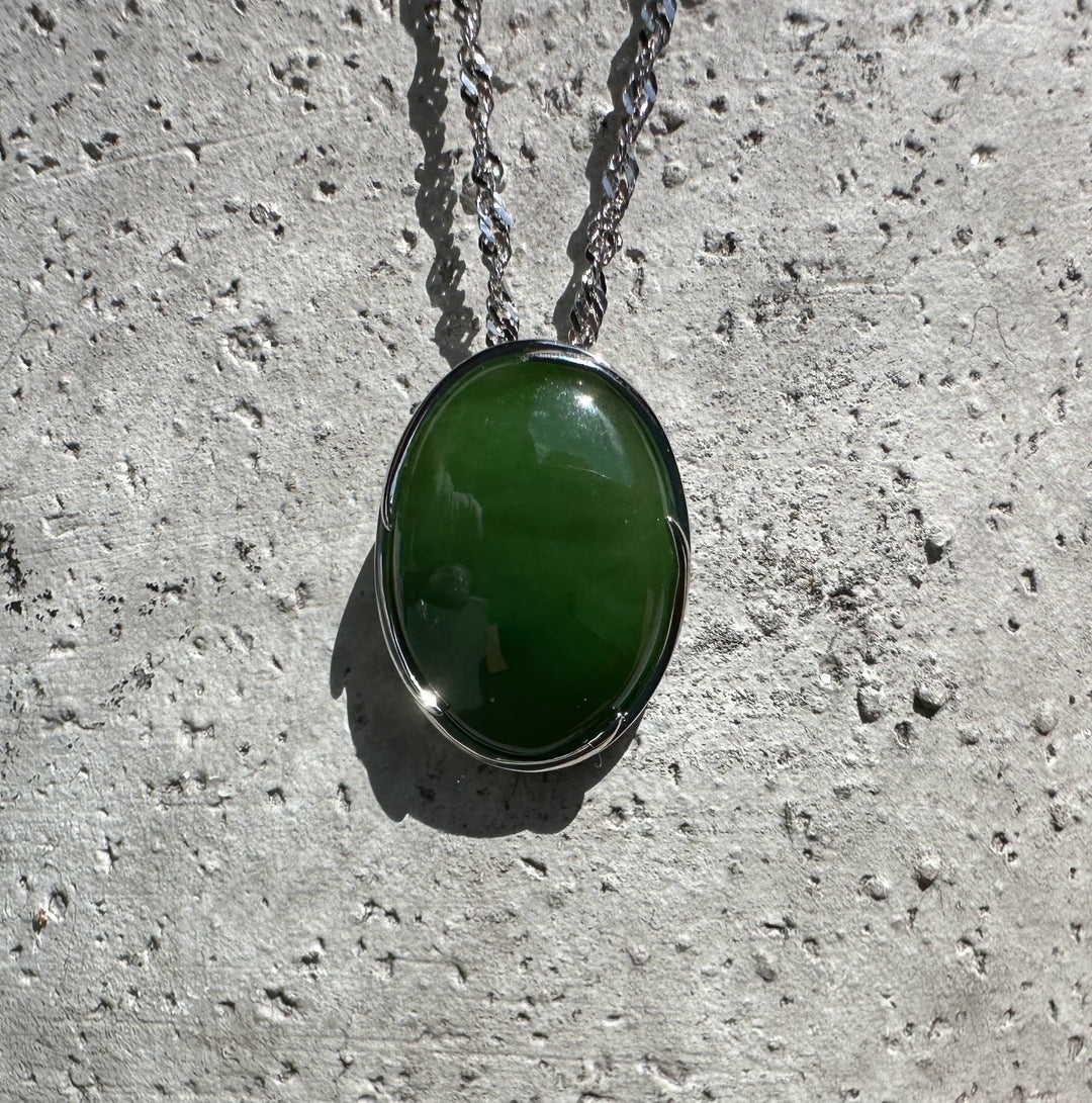 Oval bright green jade pendant in a silver bezel with chain against a concrete backdrop