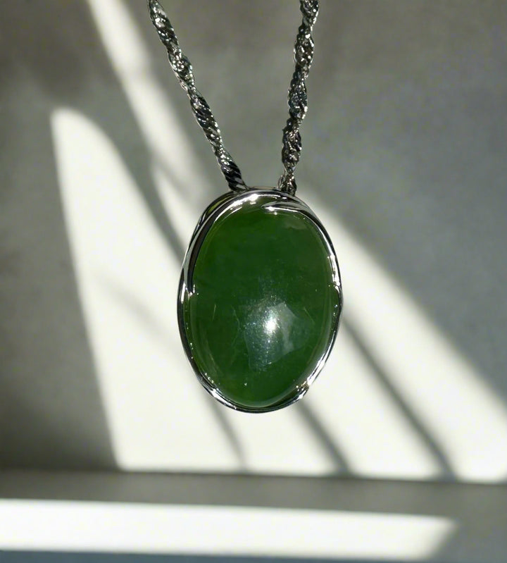 Oval bright green jade pendant suspended from a twisted silver chain against a light background.