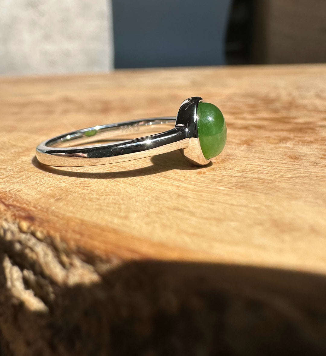 Side view of a jade and silver ring with a green cabochon bezel on a wooden surface