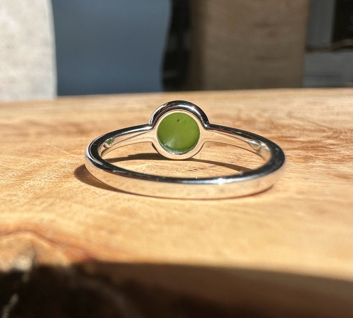 Close up of jade and silver ring showing a green round cabochon set in a silver bezel on wood