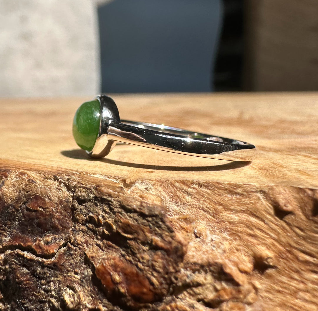 Jade and silver ring with a round green jade cabochon in a bezel on a wooden surface