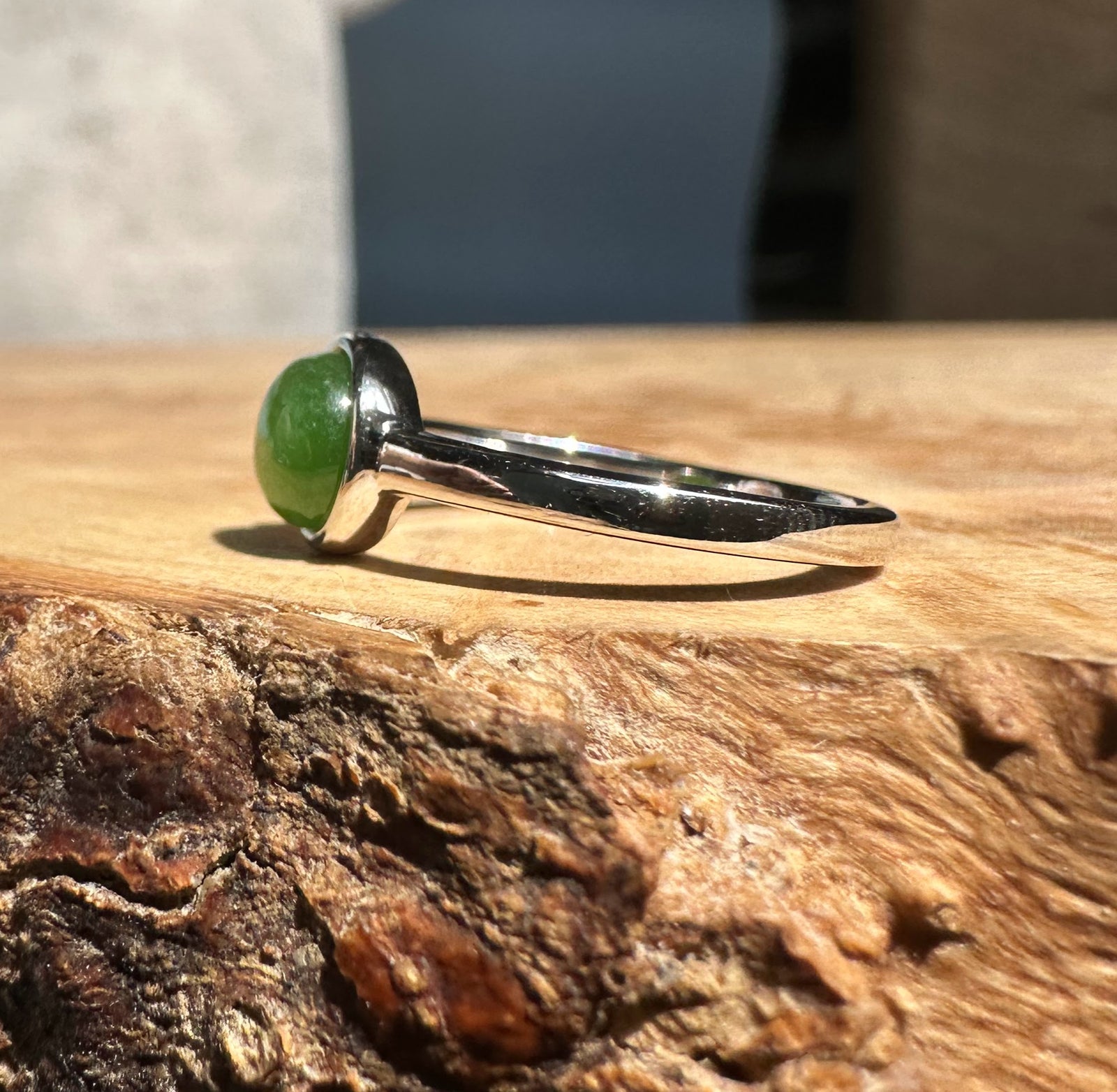 Jade and silver ring with a round green jade cabochon in a bezel on a wooden surface