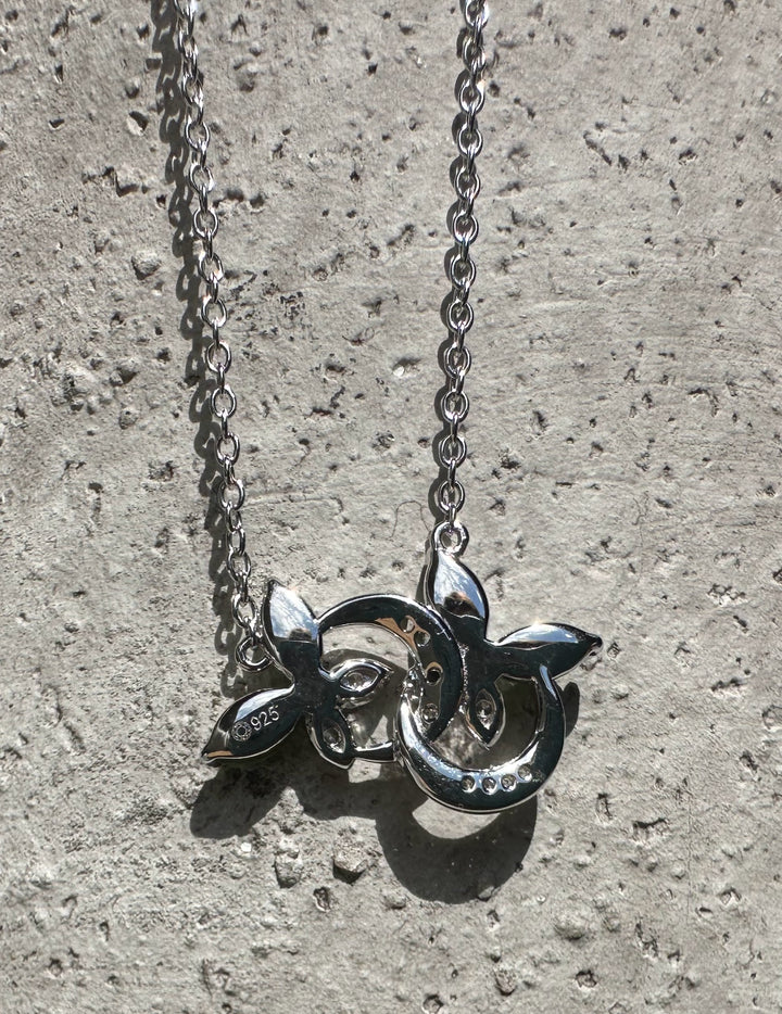 Back view of silver butterfly pendant showing 925 stamp and hollow decorative design against a stone surface.