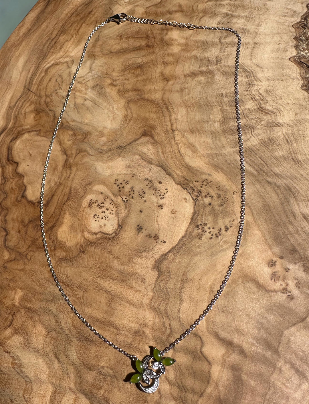 Silver butterfly pendant necklace featuring green leaf accents on a delicate chain against a wooden surface