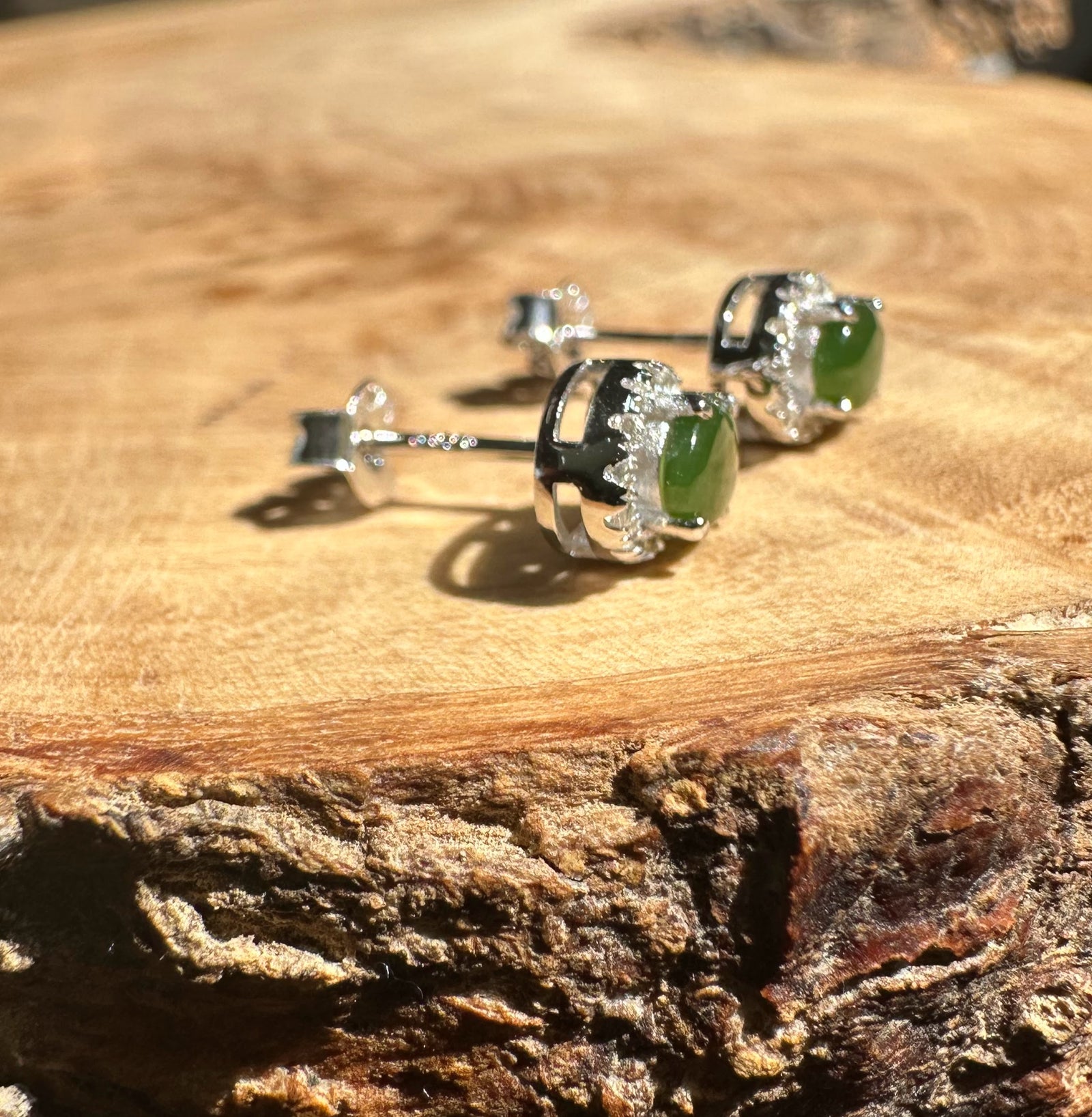Three silver jade stud earrings with oval green stones arranged on a wooden surface.