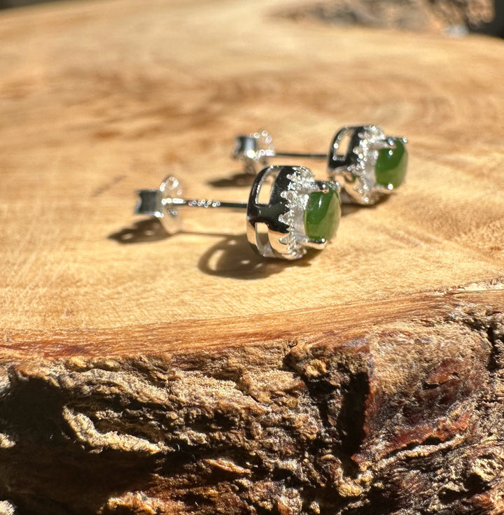 Three silver jade stud earrings with oval green stones arranged on a wooden surface.