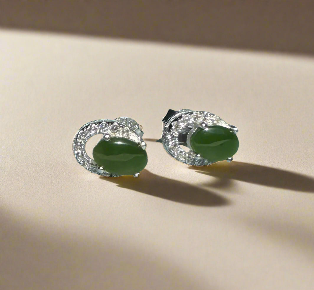 Pair of Silver Jade Studs with green oval centers and diamond halos resting on a light surface