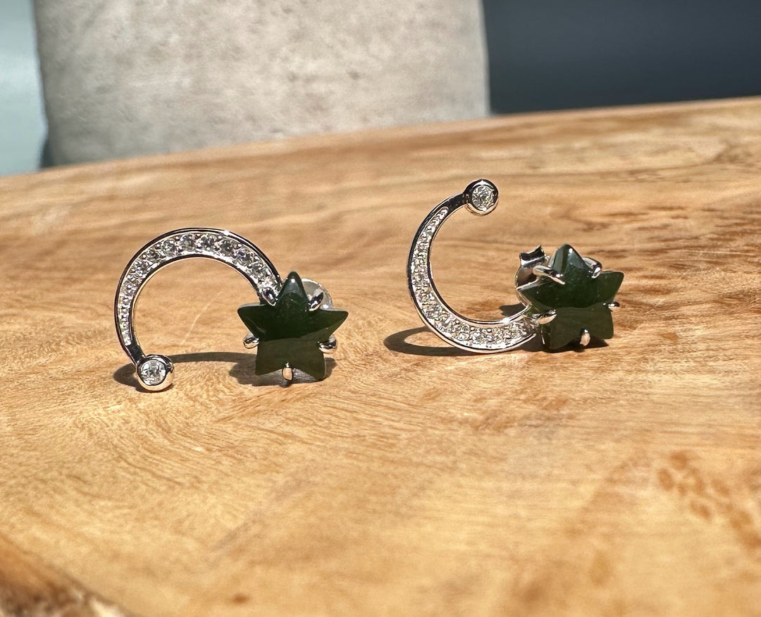 Two silver crescent moon studs with sparkling crystals and green stars shown on a wooden table