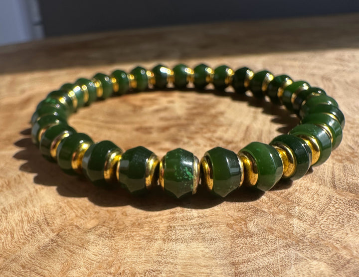 Dark green Canadian jade bead bracelet with gold spacer beads on a wooden surface