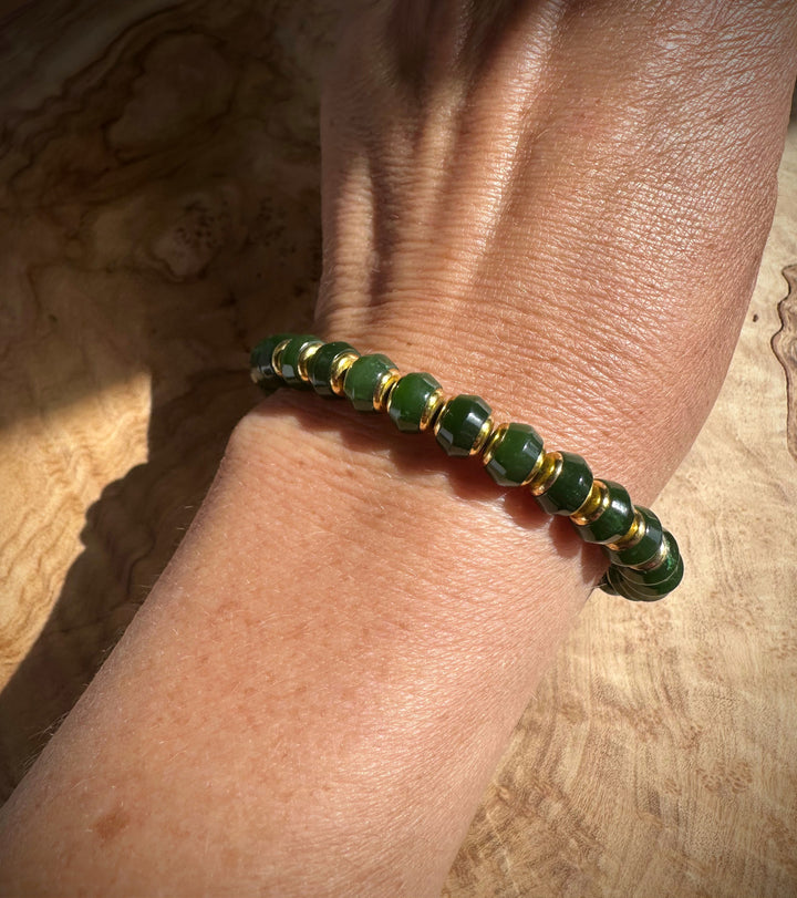 Close up of dark green jade beads with gold spacers around the wrist.