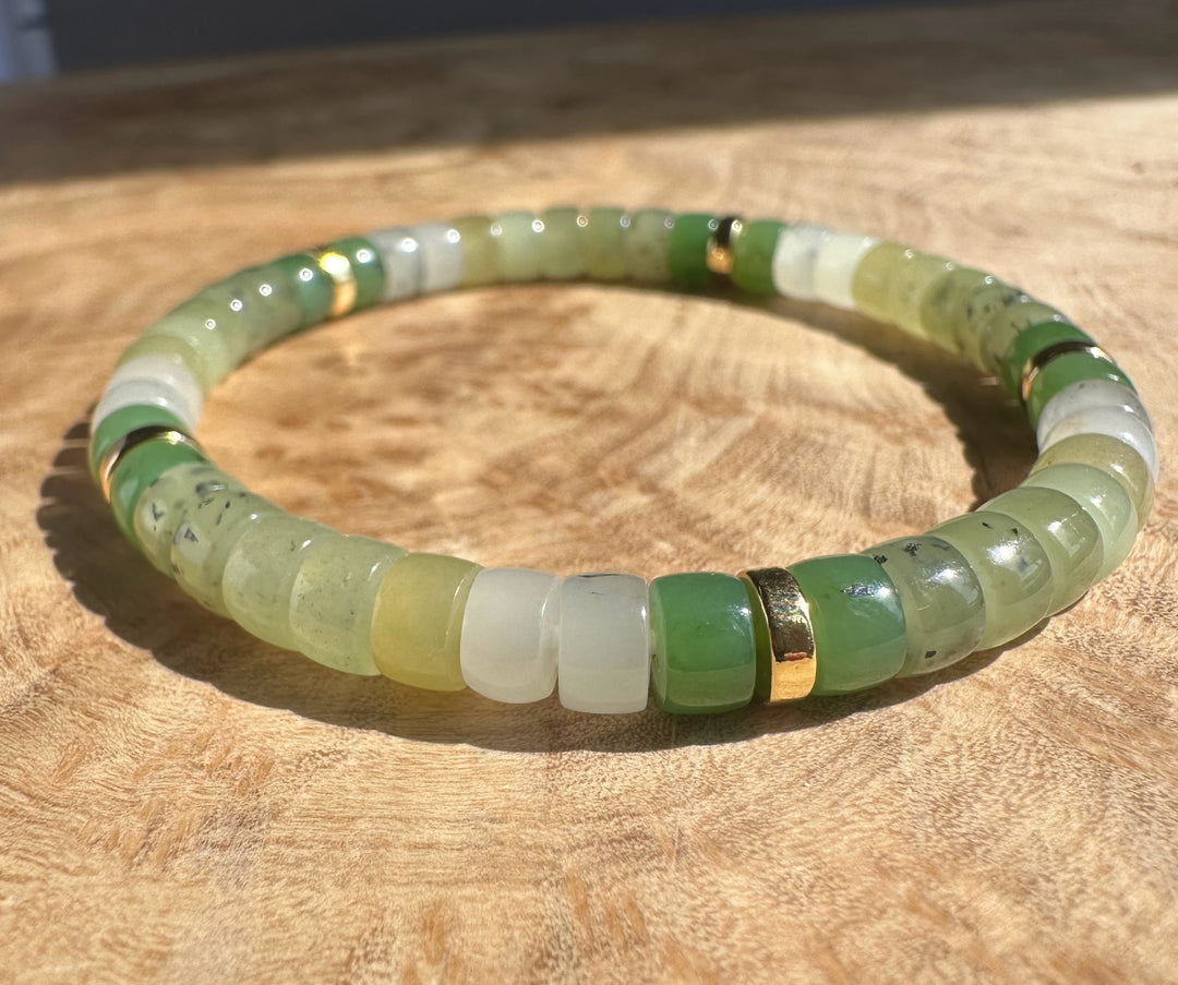 Natural multi color nephrite jade rondelle bracelet with light green beads and gold spacers on a wooden surface.