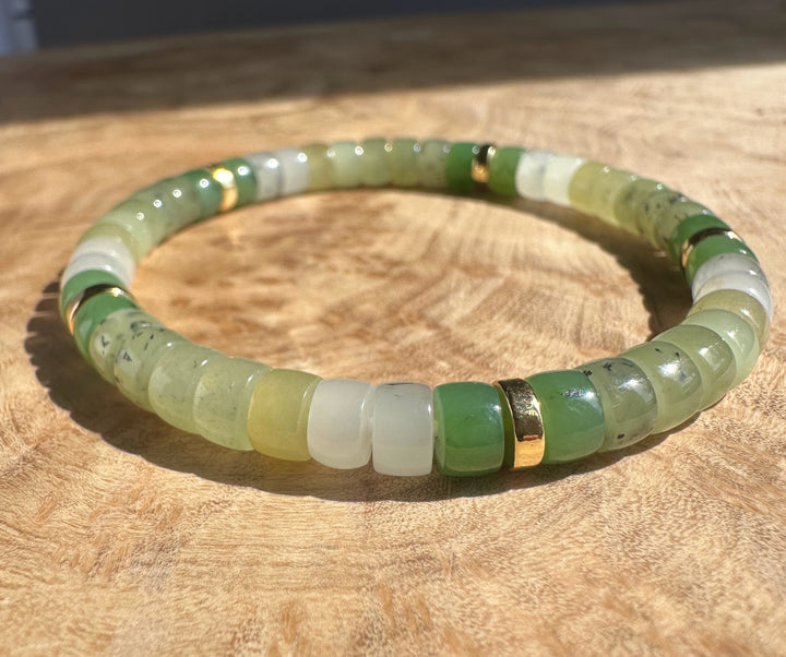 Natural multi color nephrite jade rondelle bracelet with light green beads and gold spacers on a wooden surface.
