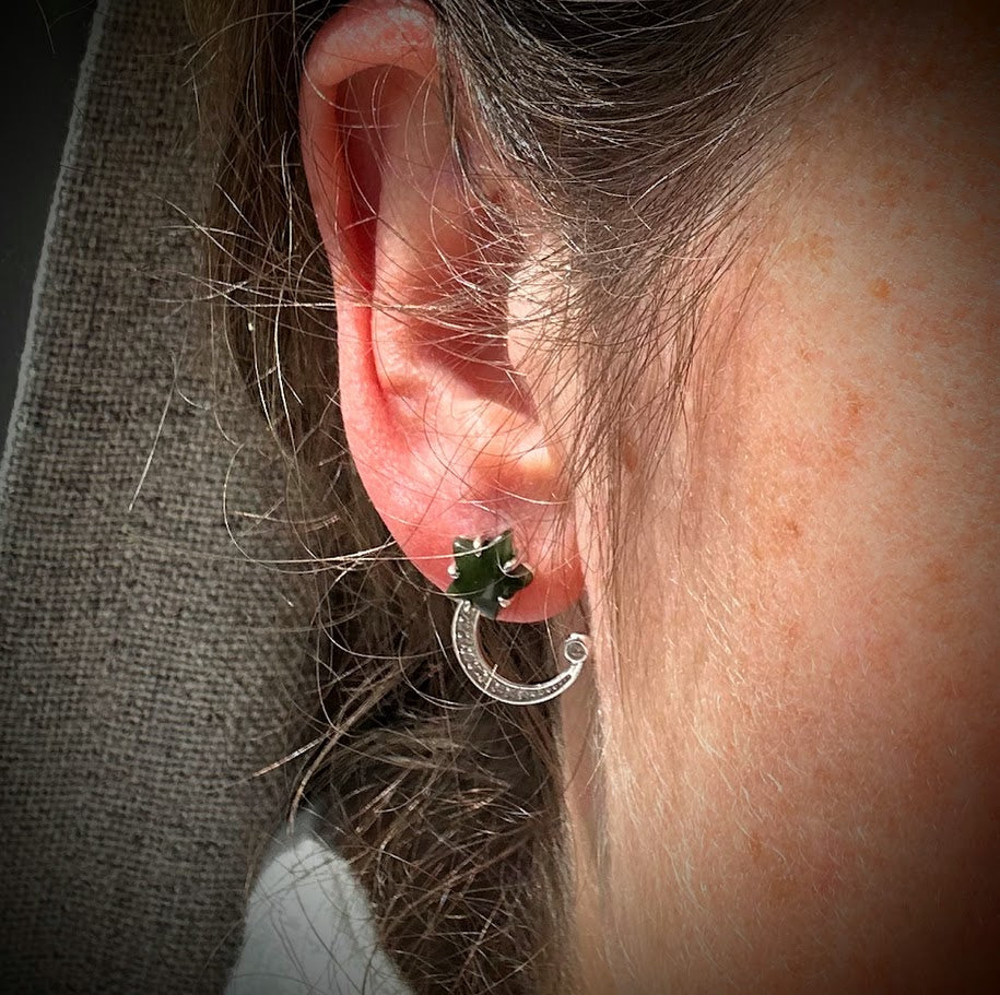 Ear with a silver crescent moon hoop encrusted with stones and a small green star stud.