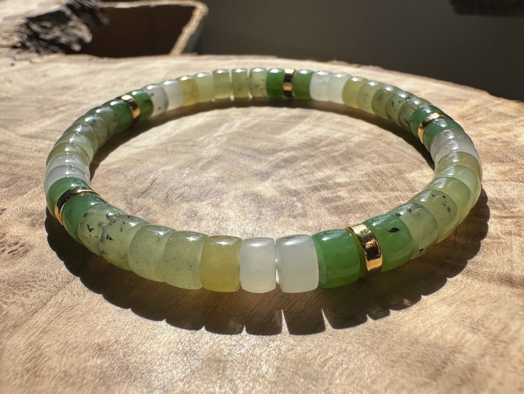 Natural multi color nephrite jade rondelle bracelet with gold spacers on a wooden surface.