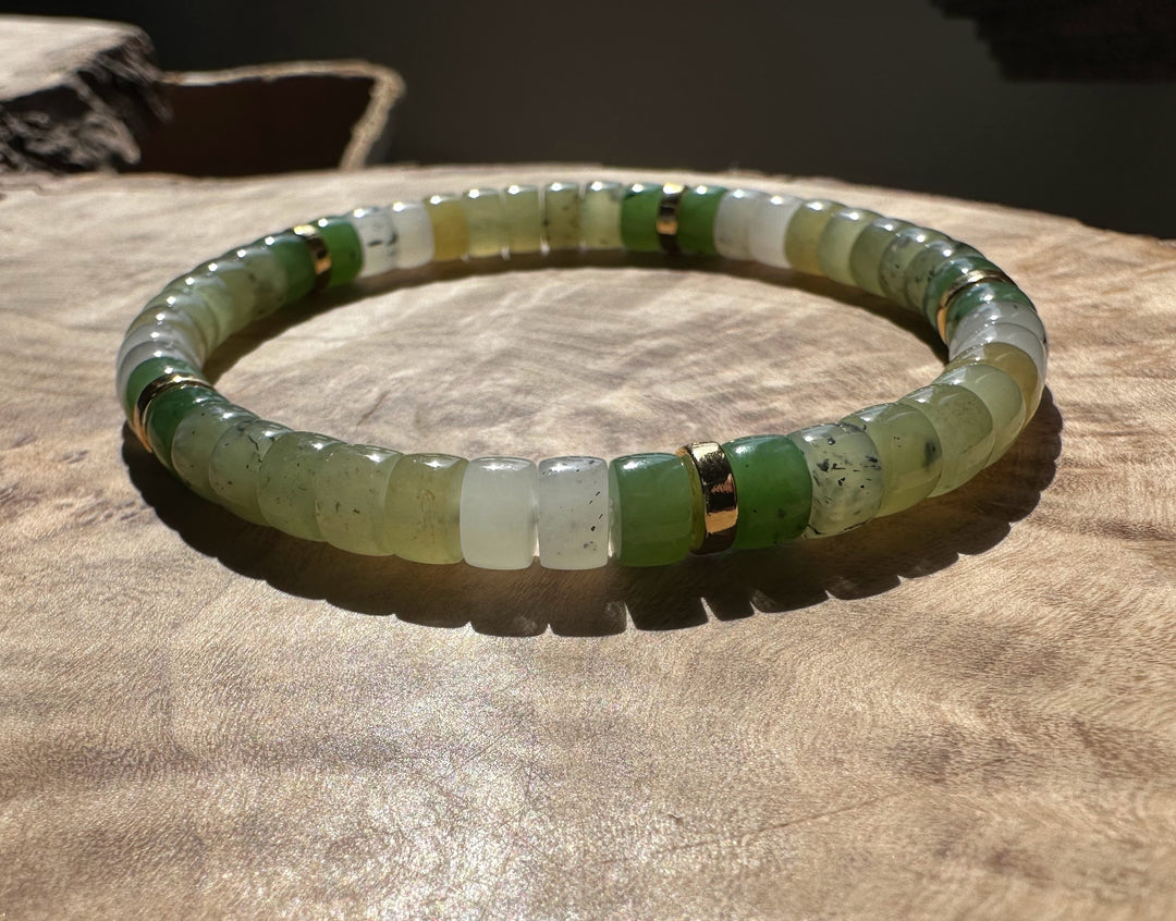 Natural multi color nephrite jade rondelle bracelet with pale green and white beads and gold spacers on a wooden surface.