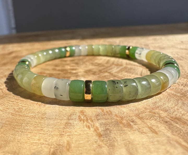 Natural nephrite jade rondelle bracelet in green and cream tones with gold spacers on a wooden surface