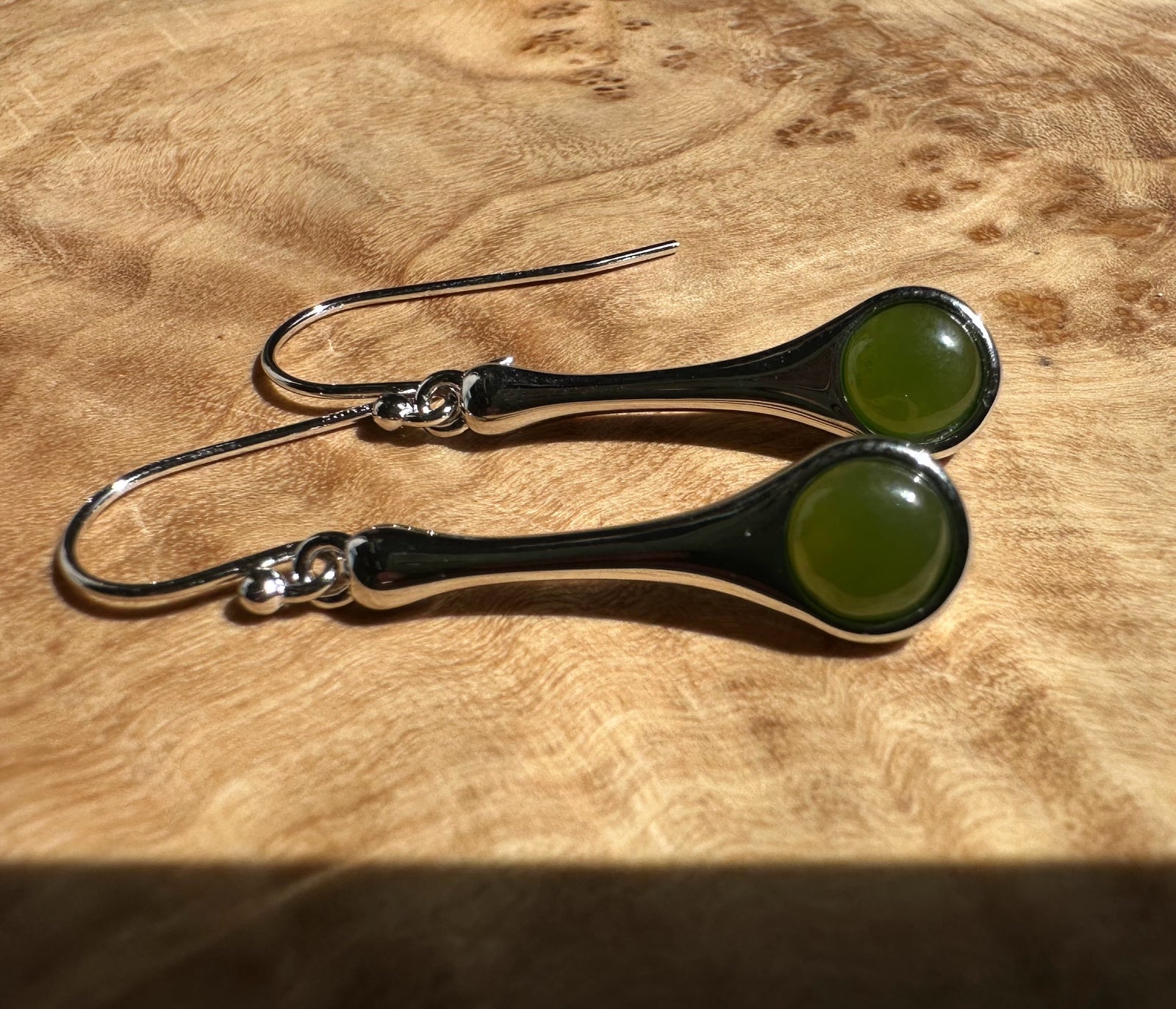 Silver drop earrings featuring curved stems and green round cabochon stones